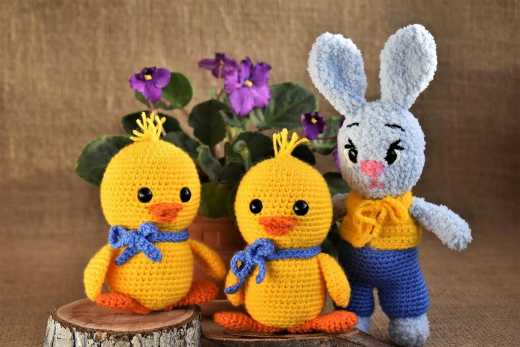 Charming crochet ducklings and bunny with vibrant purple flowers on burlap.