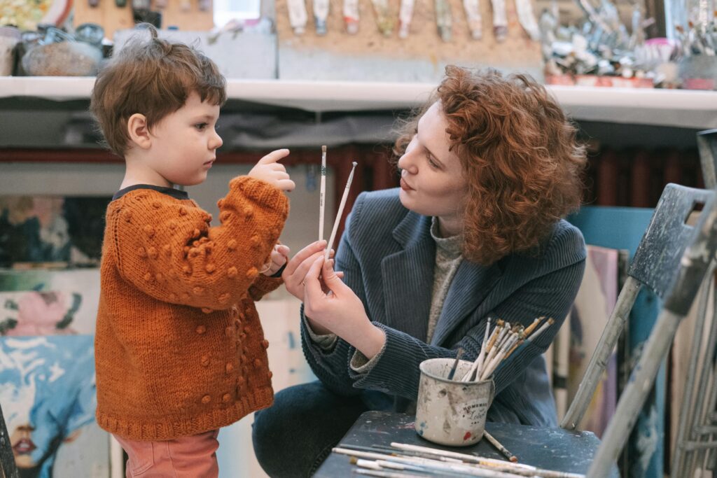 A mother and her young child painting together in a cozy art studio setting.