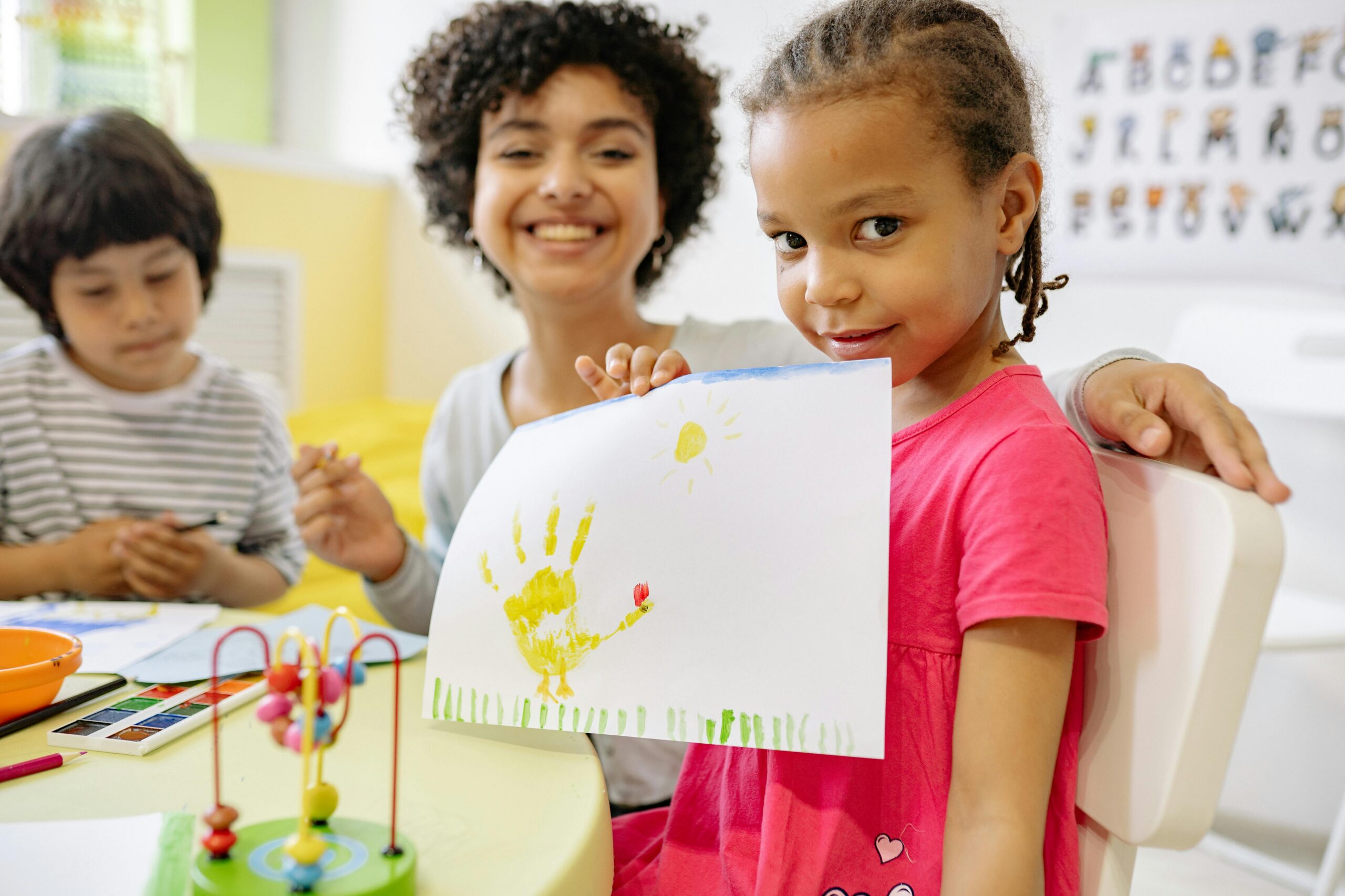 Kids enjoying creative painting activities with teacher in a cheerful classroom setting.
